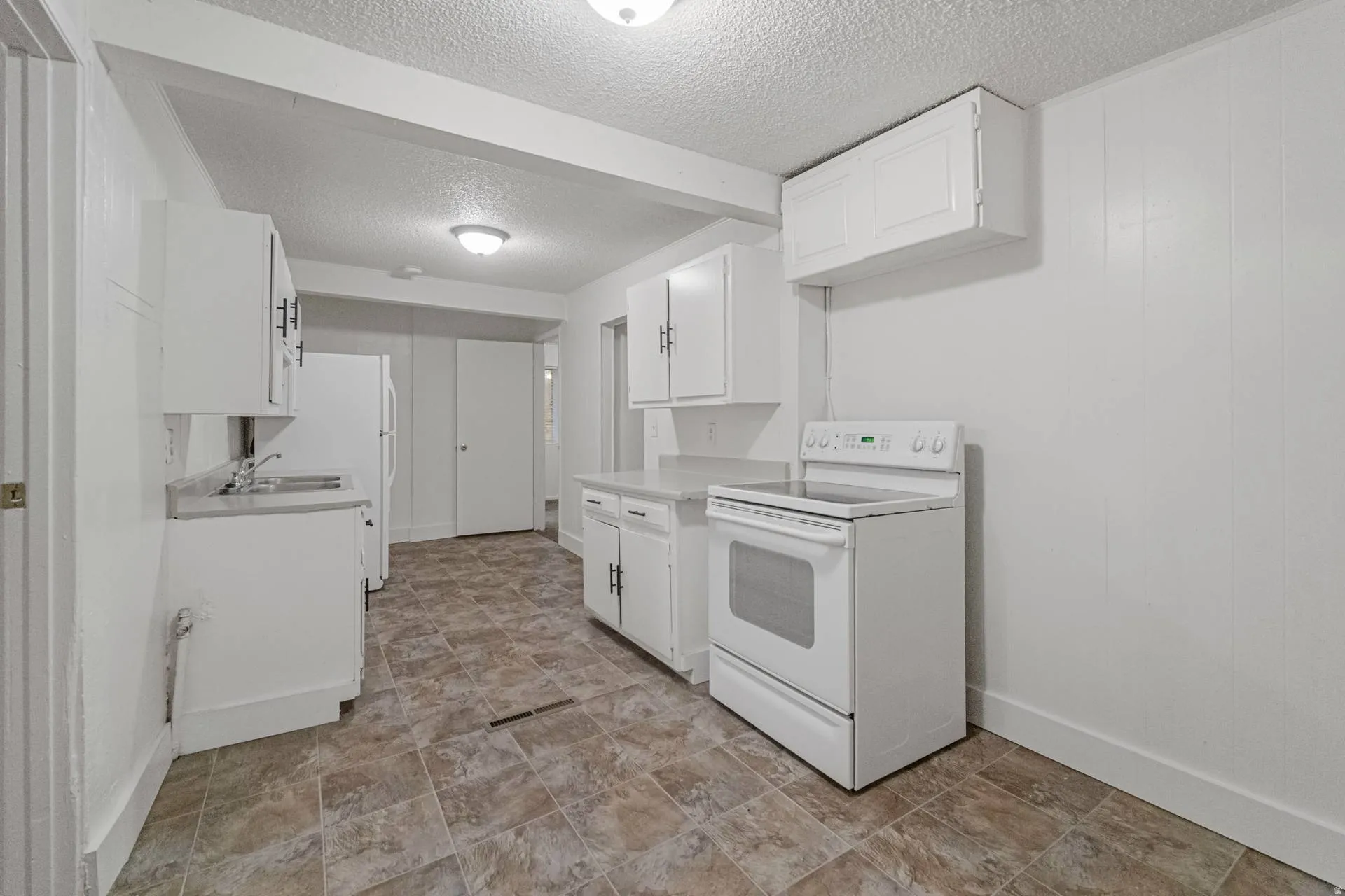Kitchen featuring white cabinetry, a built-in range, a stainless steel sink, light-colored countertops, and patterned tile flooring
