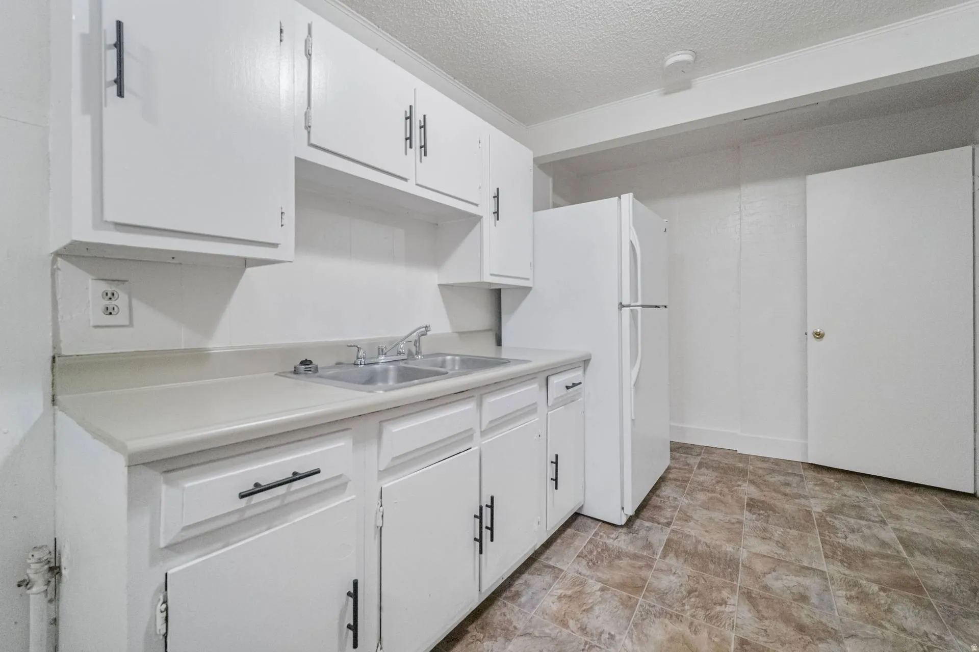 White upper and lower cabinetry, dual basin stainless steel sink, light-toned countertop, white refrigerator, and patterned floor tiling
