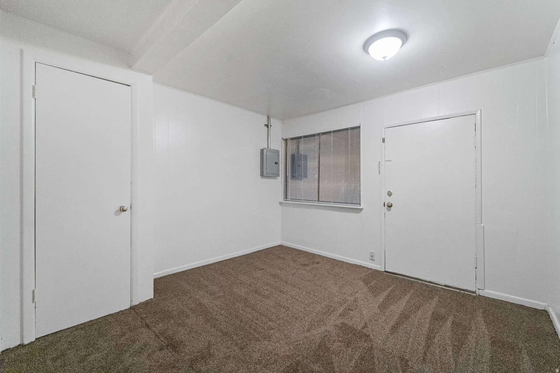 Carpeted room with a flush-mount ceiling light fixture, white paneled walls, and a window with horizontal panes