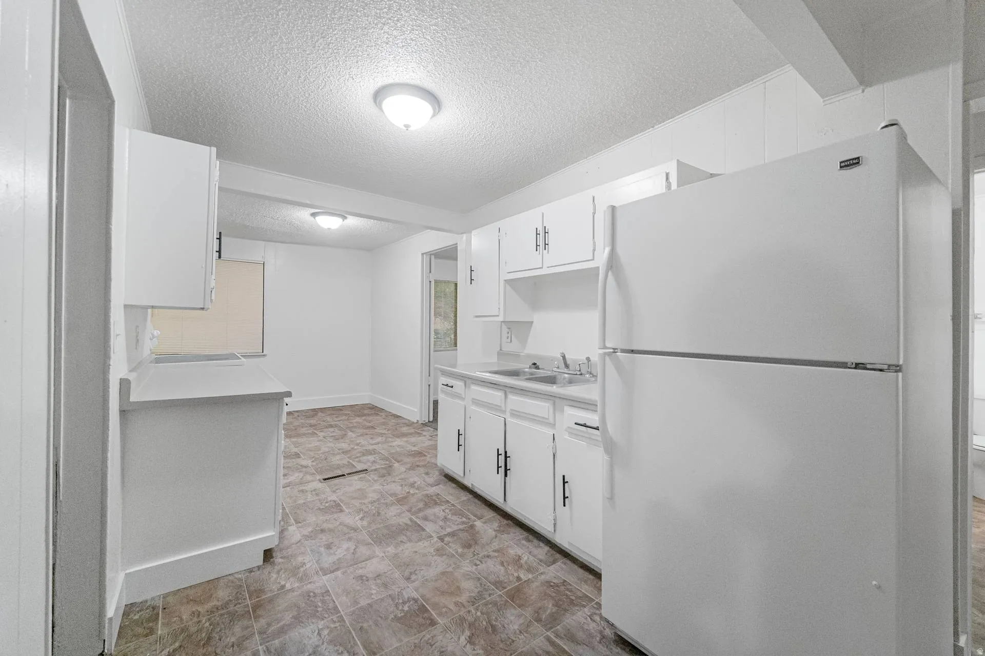 Kitchen featuring white cabinetry with black hardware, laminate countertops, a double basin sink, and tile-look flooring