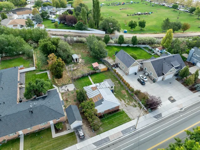 Aerial perspective showcasing multiple properties, extensive paved driveways, a detached garage, and a large grassy area