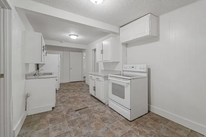 Kitchen featuring white cabinetry, a built-in range, a stainless steel sink, light-colored countertops, and patterned tile flooring