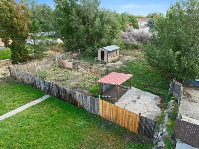 Backyard featuring a partially fenced area with a small shed and a covered concrete pad