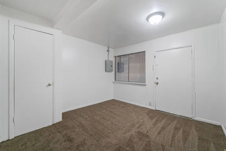 Carpeted room with a flush-mount ceiling light fixture, white paneled walls, and a window with horizontal panes