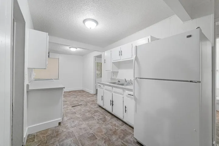 Kitchen featuring white cabinetry with black hardware, laminate countertops, a double basin sink, and tile-look flooring
