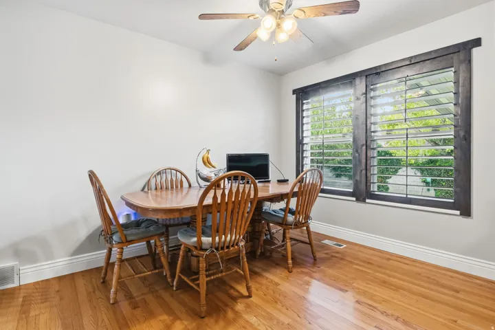 Hardwood flooring, white wall paint, dark wood window trim, louvered window blinds, and a ceiling fan with integrated lighting