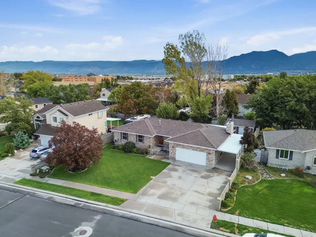 Brick veneer exterior, attached garage, extended driveway, mature landscaping, and mountain scenery