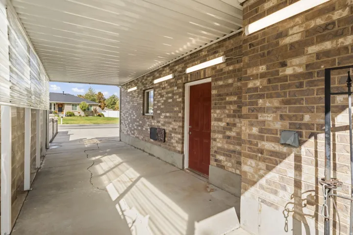 Covered concrete walkway featuring a brick exterior wall, a red entry door, and integrated overhead lighting