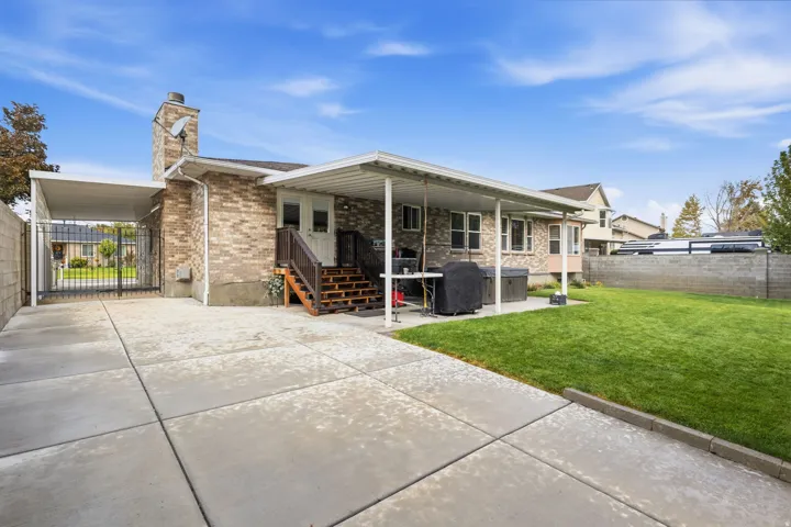 Brick exterior with a covered patio, extensive concrete driveway, and a gated side access