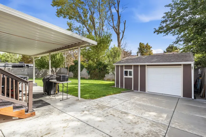 Expansive concrete patio with a covered outdoor area, leading to a detached garage with a white roll-up door