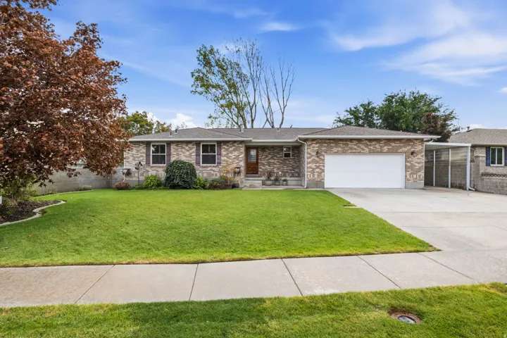 Brick exterior with a white garage door, a paved driveway, and a front yard with mature landscaping