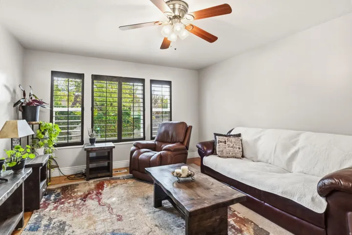 Three distinct windows with interior shutters, a ceiling fan with integrated lighting, and wood-finish flooring
