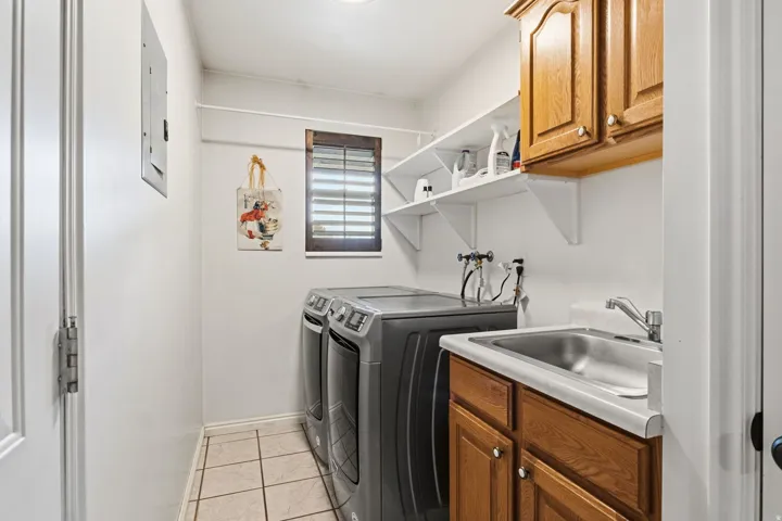 Utility room with tile flooring, a stainless steel utility sink, wood cabinetry, and open shelving