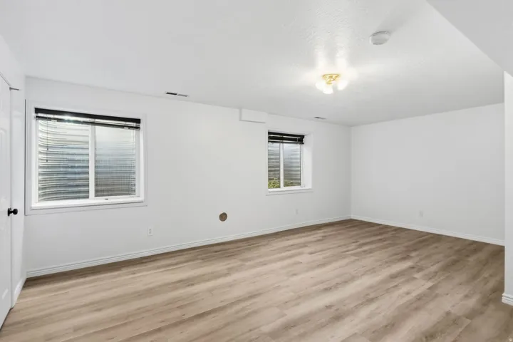 Spacious room featuring light wood-finish flooring, white walls, and two egress windows