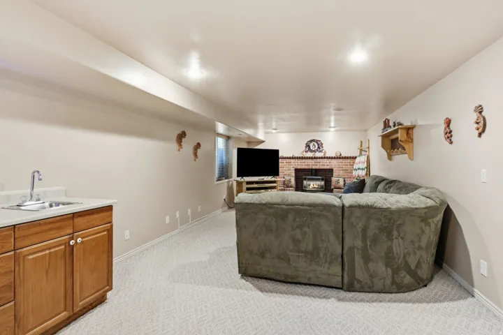 Finished lower level with a brick-faced fireplace, built-in shelving, recessed lighting, and a wet bar featuring a stainless steel sink and wood-finish cabinetry