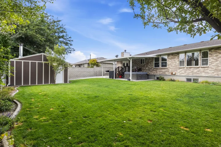 Expansive backyard featuring a manicured lawn, a detached storage shed, a covered patio, and a brick-finish exterior