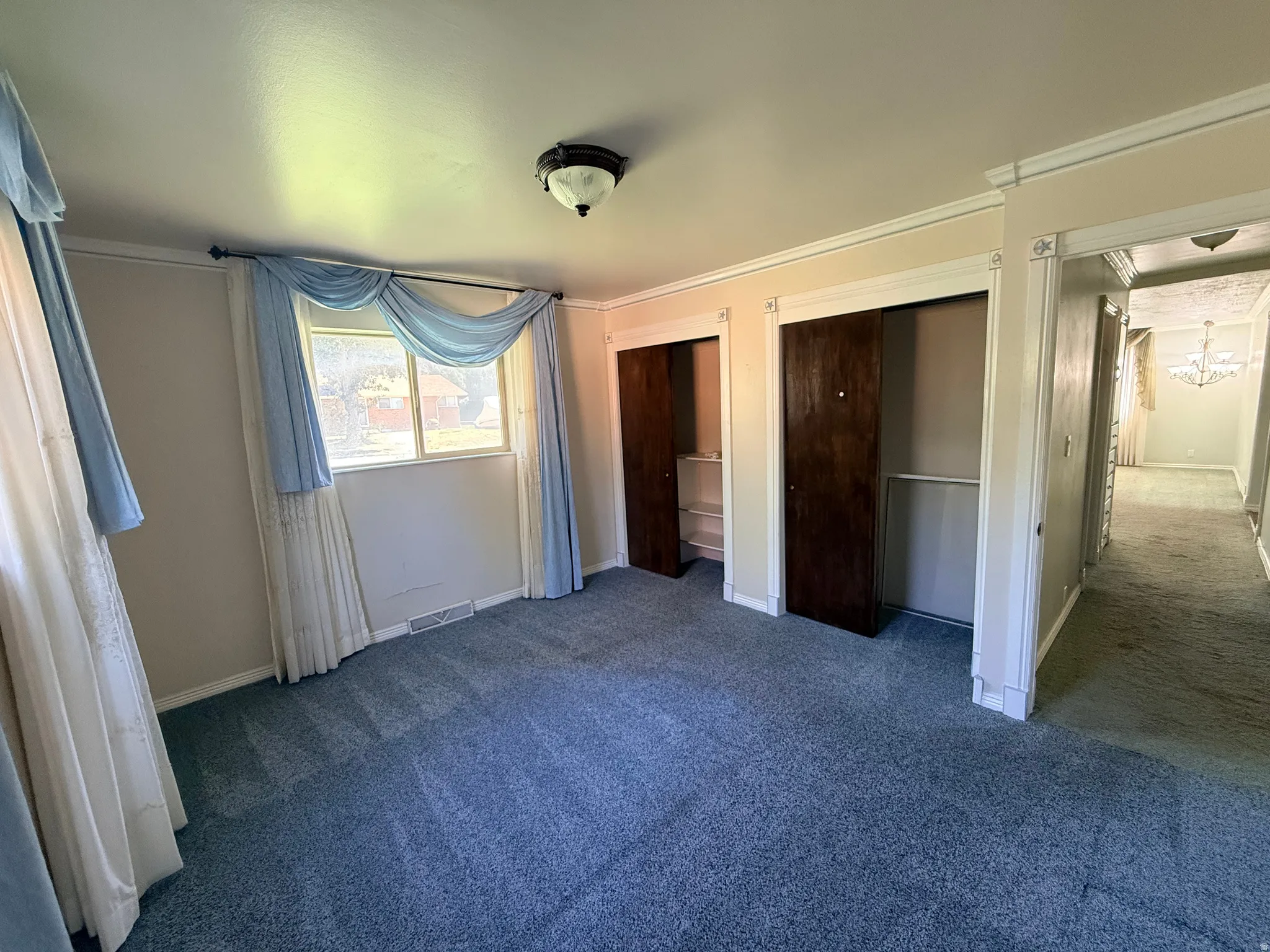 Window opening with natural light, two closet openings with dark wood-finish doors, carpet flooring, and a flush mount ceiling fixture