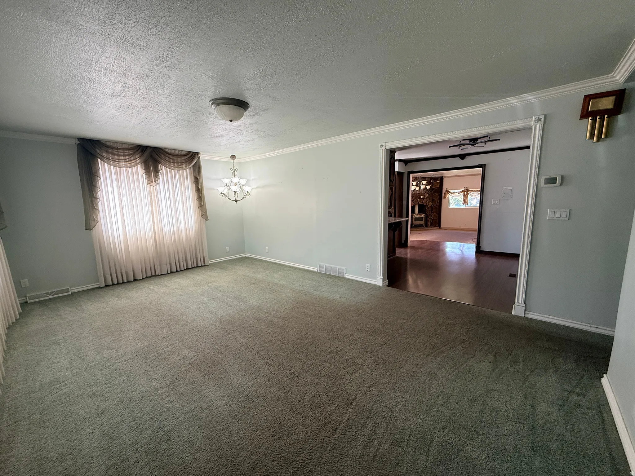 Spacious carpeted room featuring a decorative chandelier, crown molding, and a wide doorway