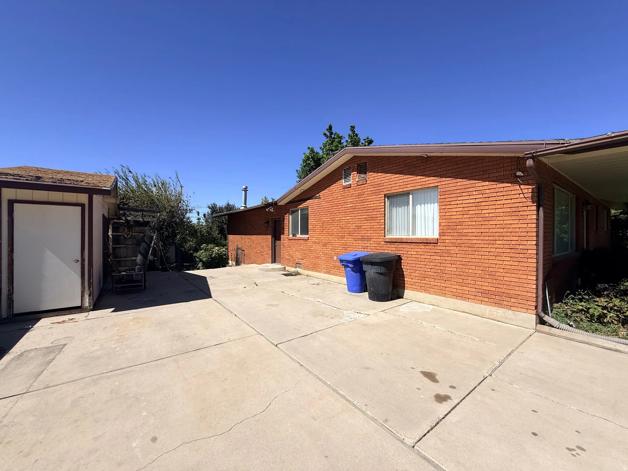 Red brick exterior with white trim windows, concrete patio, and attached carport