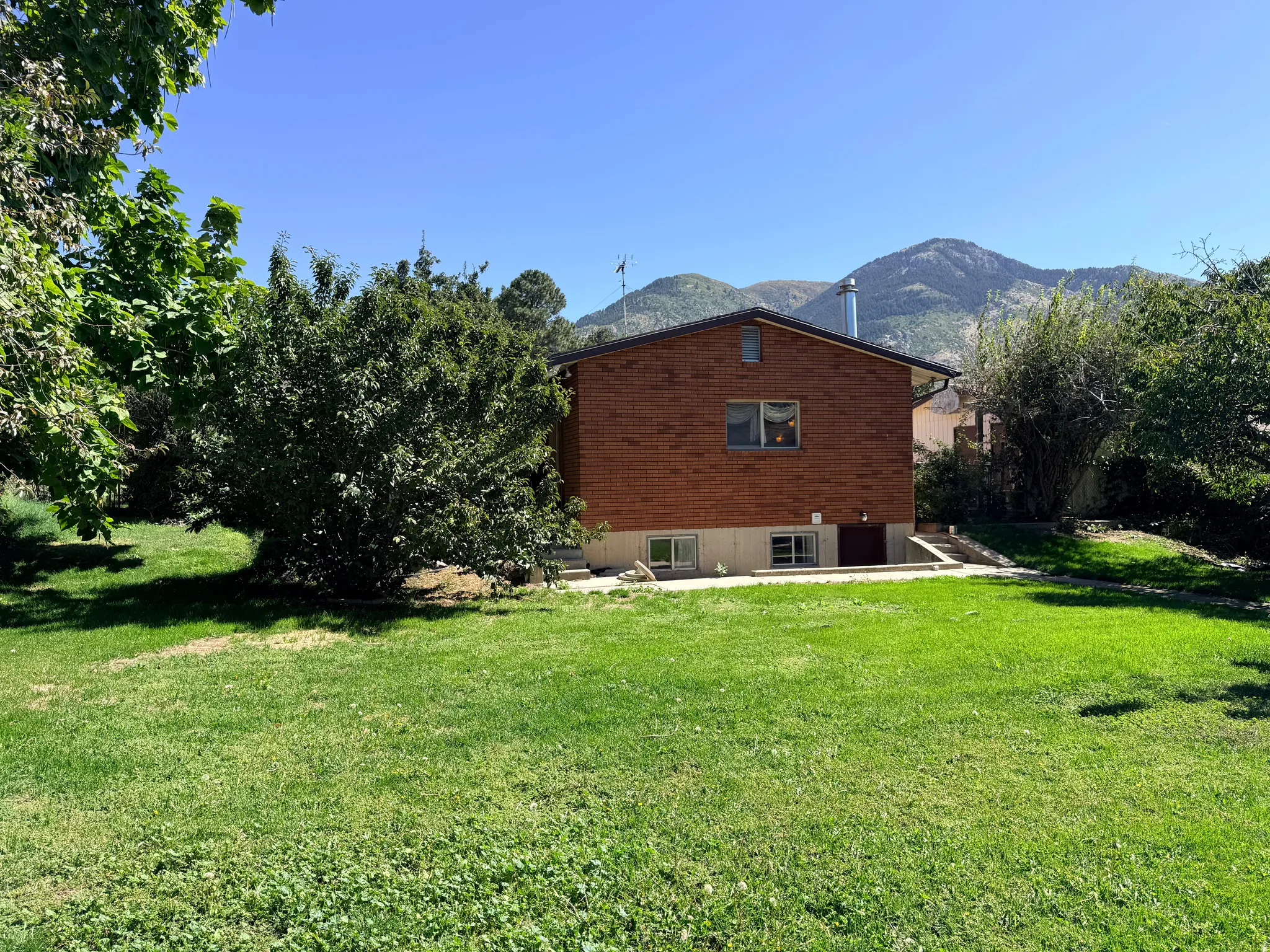 Expansive green lawn with mature landscaping and mountain backdrop