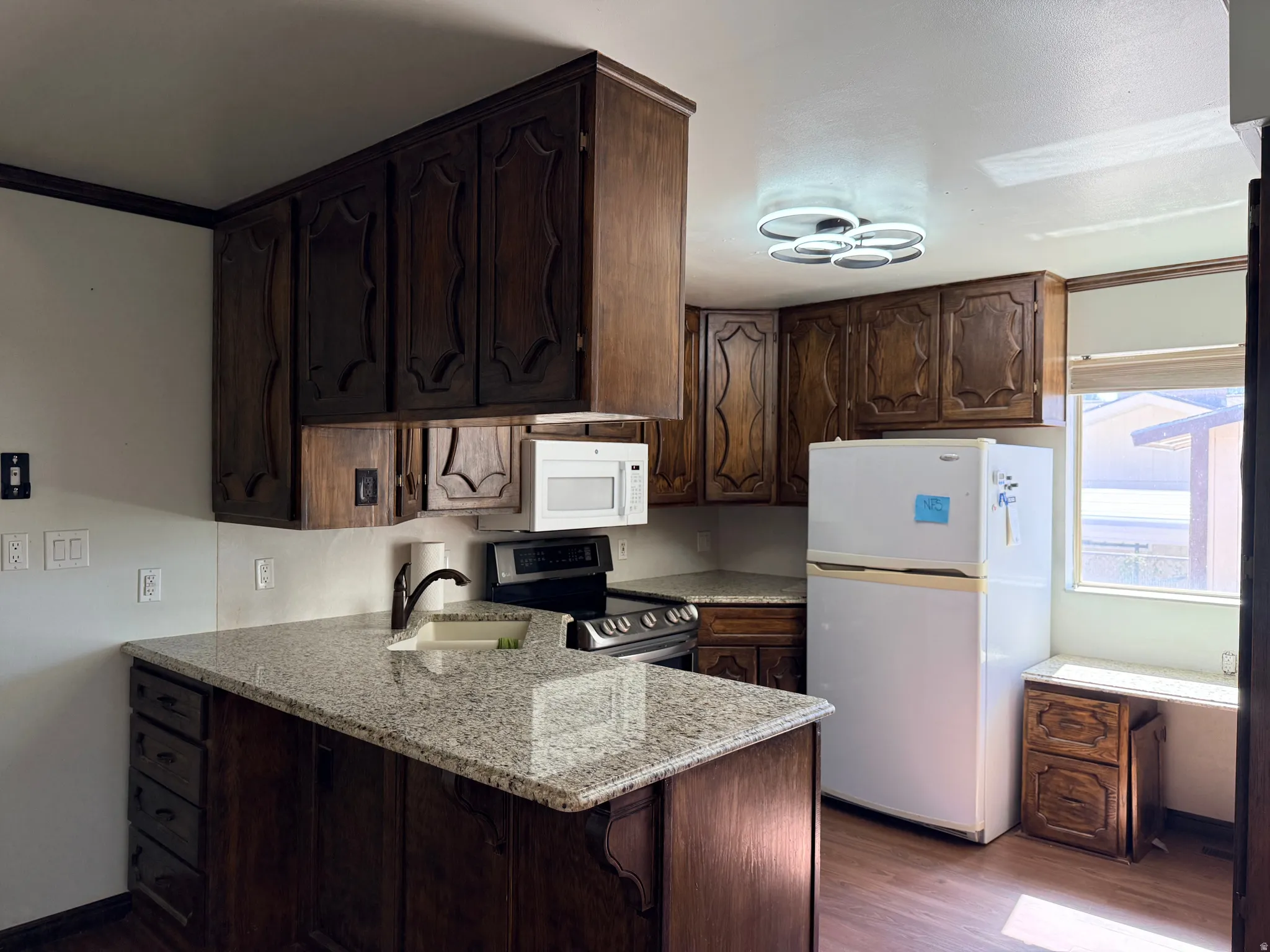 Dark wood cabinetry, speckled countertops, built-in microwave, dark wood-finish flooring, and a modern ceiling light fixture