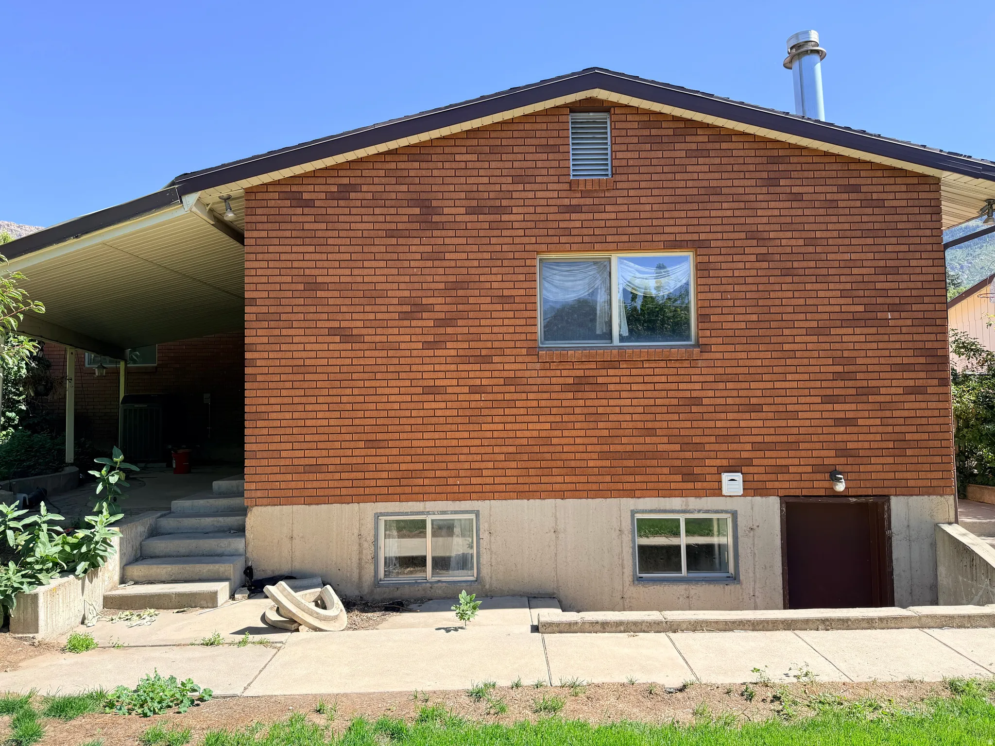 Brick exterior with a covered patio, concrete stairs, and a visible basement entrance