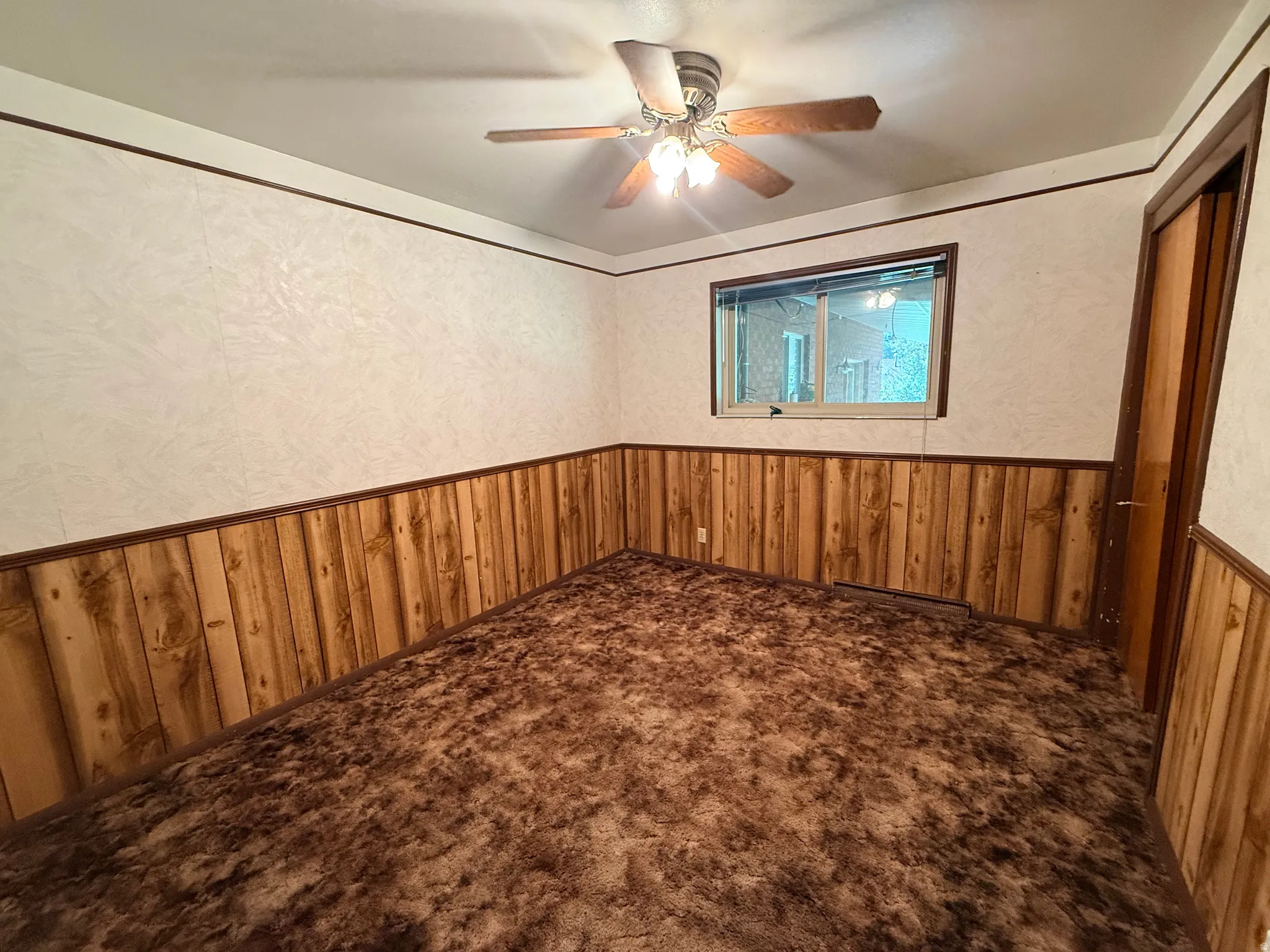 Wall-to-wall carpeting, wood paneling, a ceiling fan with integrated lighting, and a window providing natural light