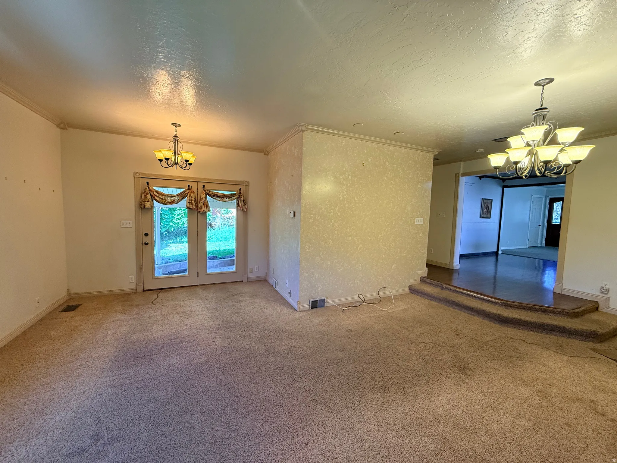 Carpeted living area with crown molding, double French doors, and an overhead chandelier