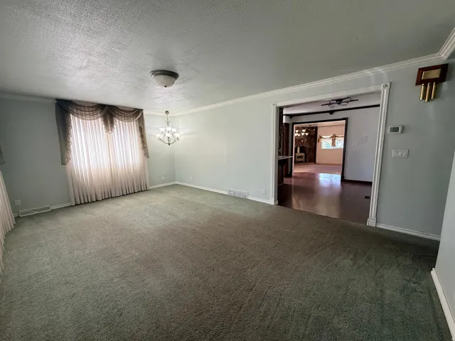 Spacious carpeted room featuring a decorative chandelier, crown molding, and a wide doorway