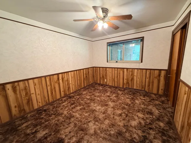 Wall-to-wall carpeting, wood paneling, a ceiling fan with integrated lighting, and a window providing natural light