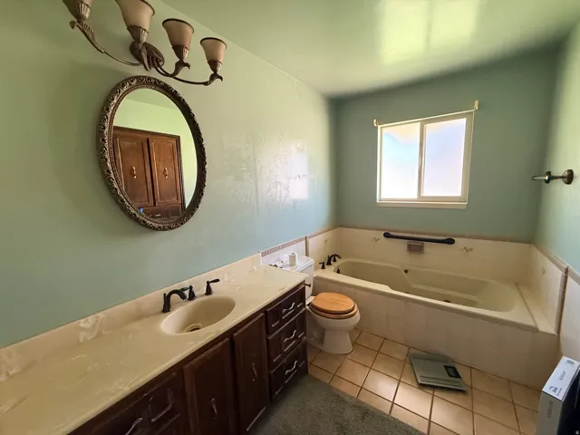 Soaking tub with tile surround, wood-finish vanity with an integrated sink, frosted window, and an oval vanity mirror with decorative frame