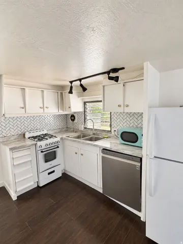 White cabinetry, herringbone tile backsplash, integrated double basin sink, stainless steel dishwasher, and wood-finish flooring