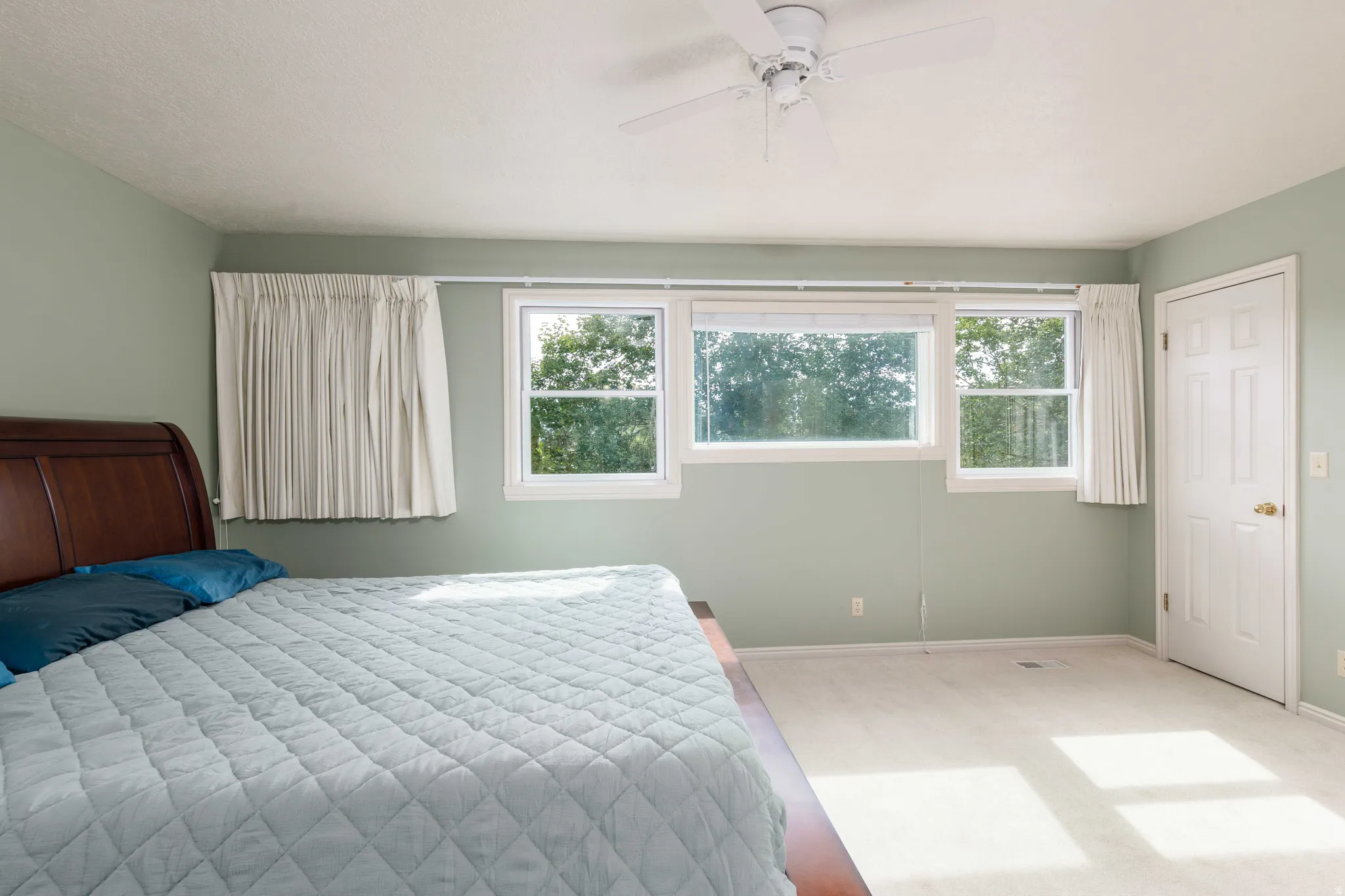Spacious room featuring multiple windows, light-colored carpeting, a ceiling fan, and a paneled door