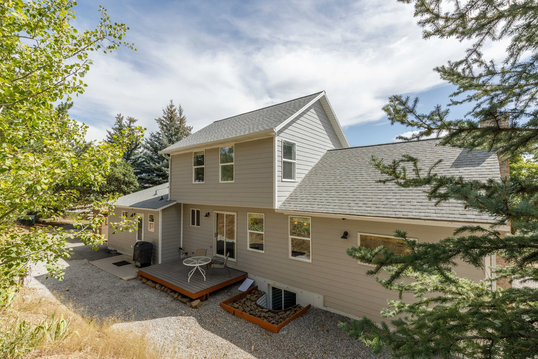 Two-story exterior with light gray siding, a gray shingle roof, and a ground-level wood-deck patio