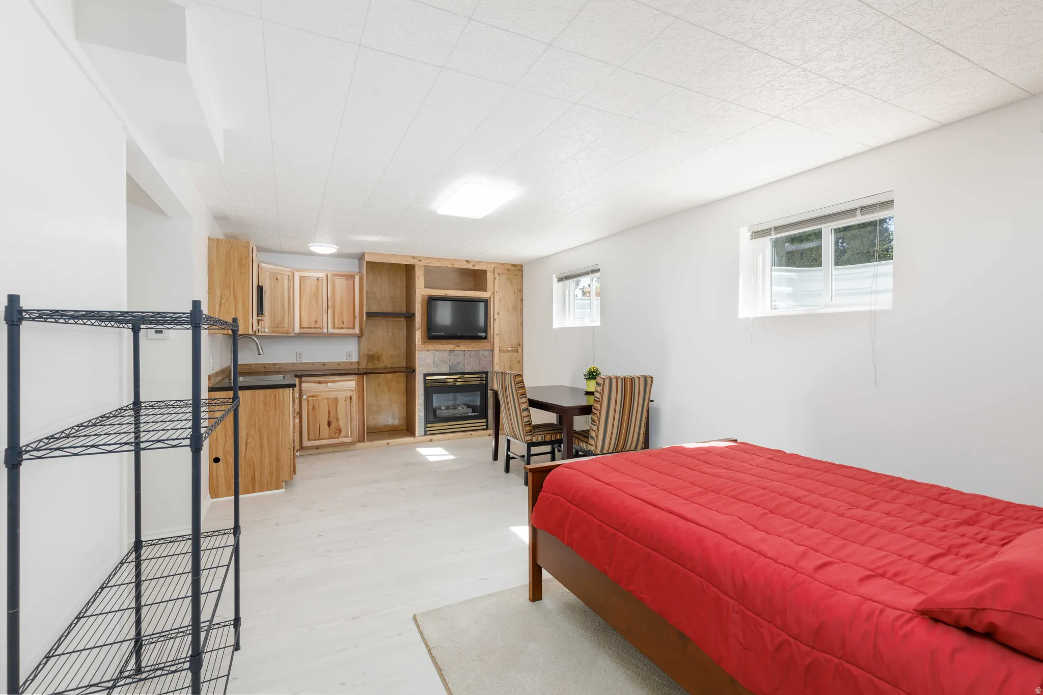 Built-in entertainment center with stone surround fireplace, dedicated kitchenette with wood cabinetry, light wood-finish flooring, and recessed lighting
