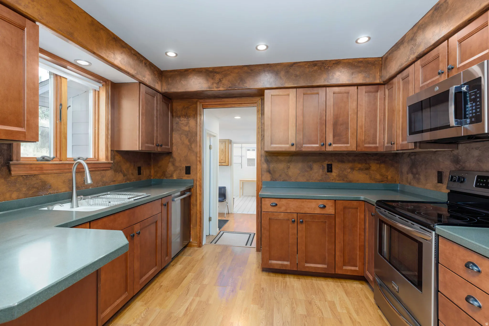 Kitchen featuring wood-finish flooring, recessed lighting, wood cabinetry, stainless steel appliances, and a stainless steel sink with a gooseneck faucet