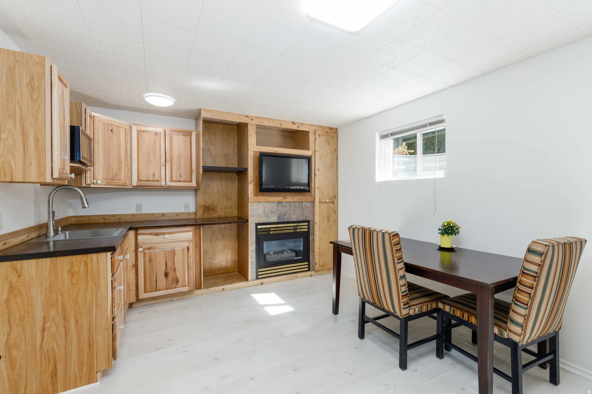 Built-in wood cabinetry with dark countertops, integrated sink with gooseneck faucet, built-in entertainment center with fireplace, and light wood-finish flooring