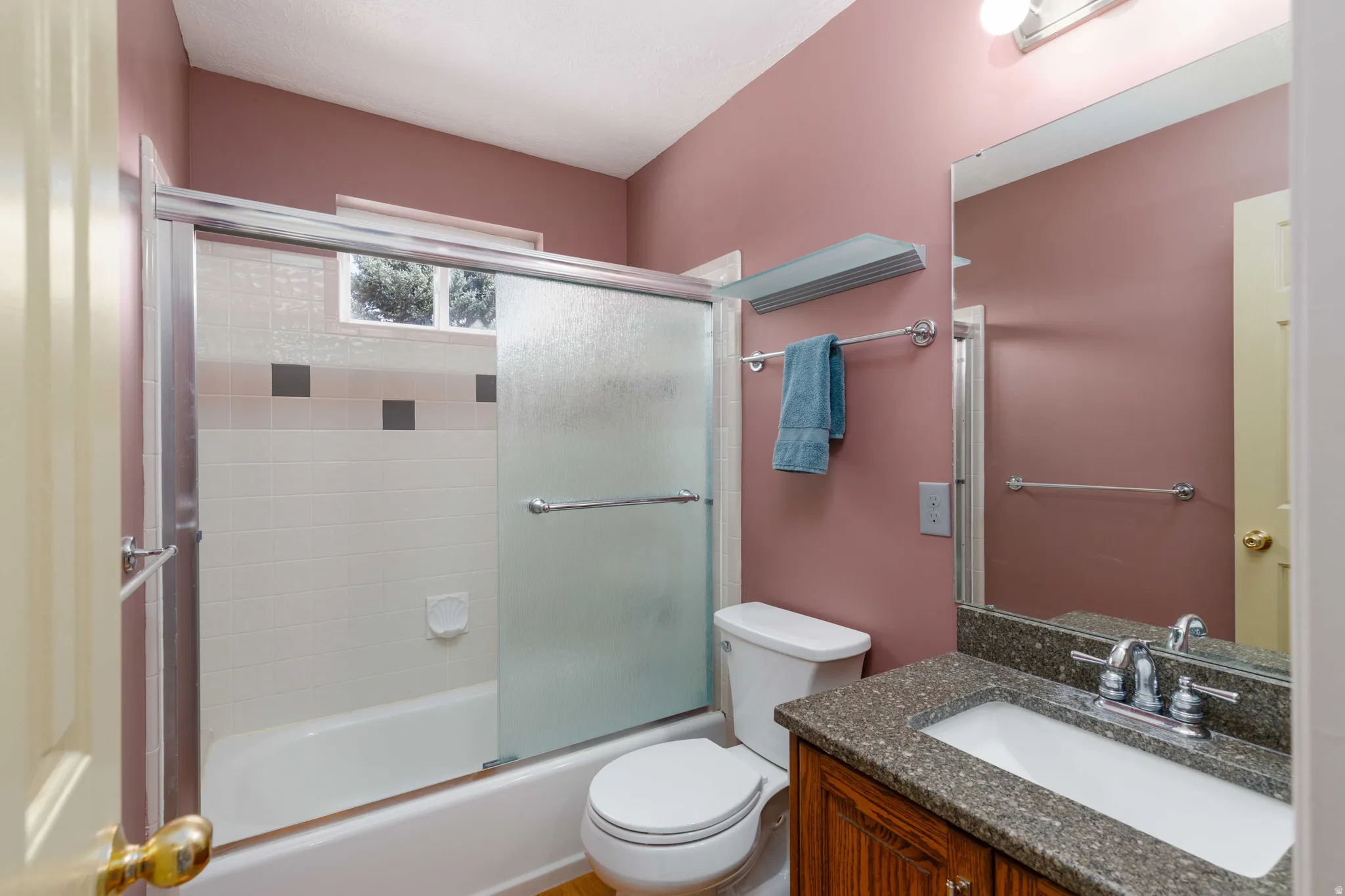 Bathtub with sliding glass shower door, integrated window, and tiled surround