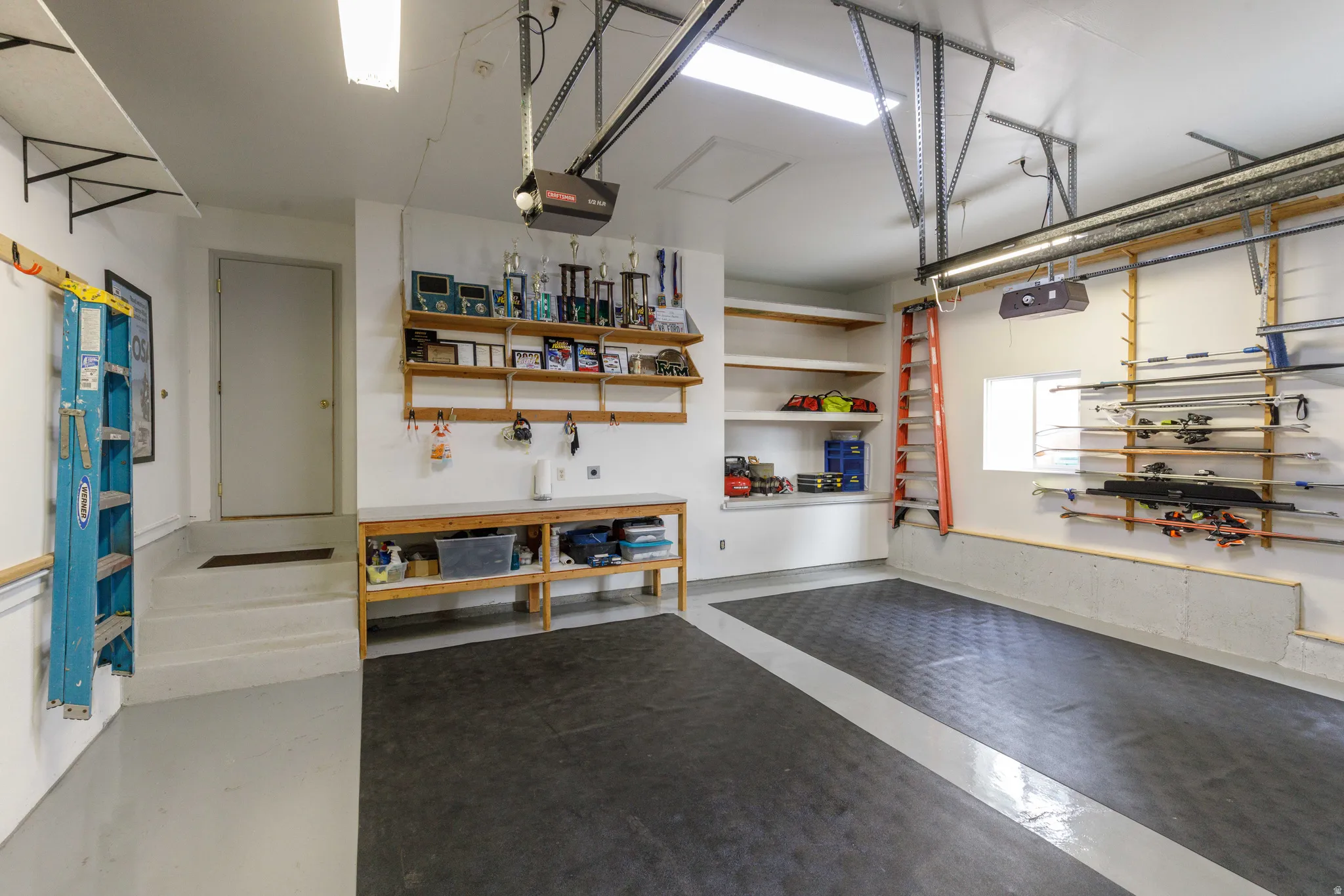Attached garage featuring a utility sink, built-in shelving, durable flooring, and fluorescent overhead lighting