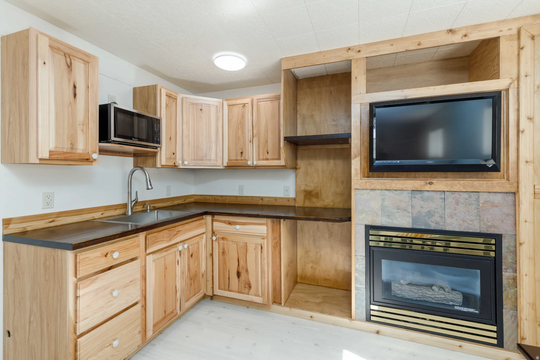 Wood-finish cabinetry, dark countertops, integrated microwave, built-in media center, and a fireplace with tile surround