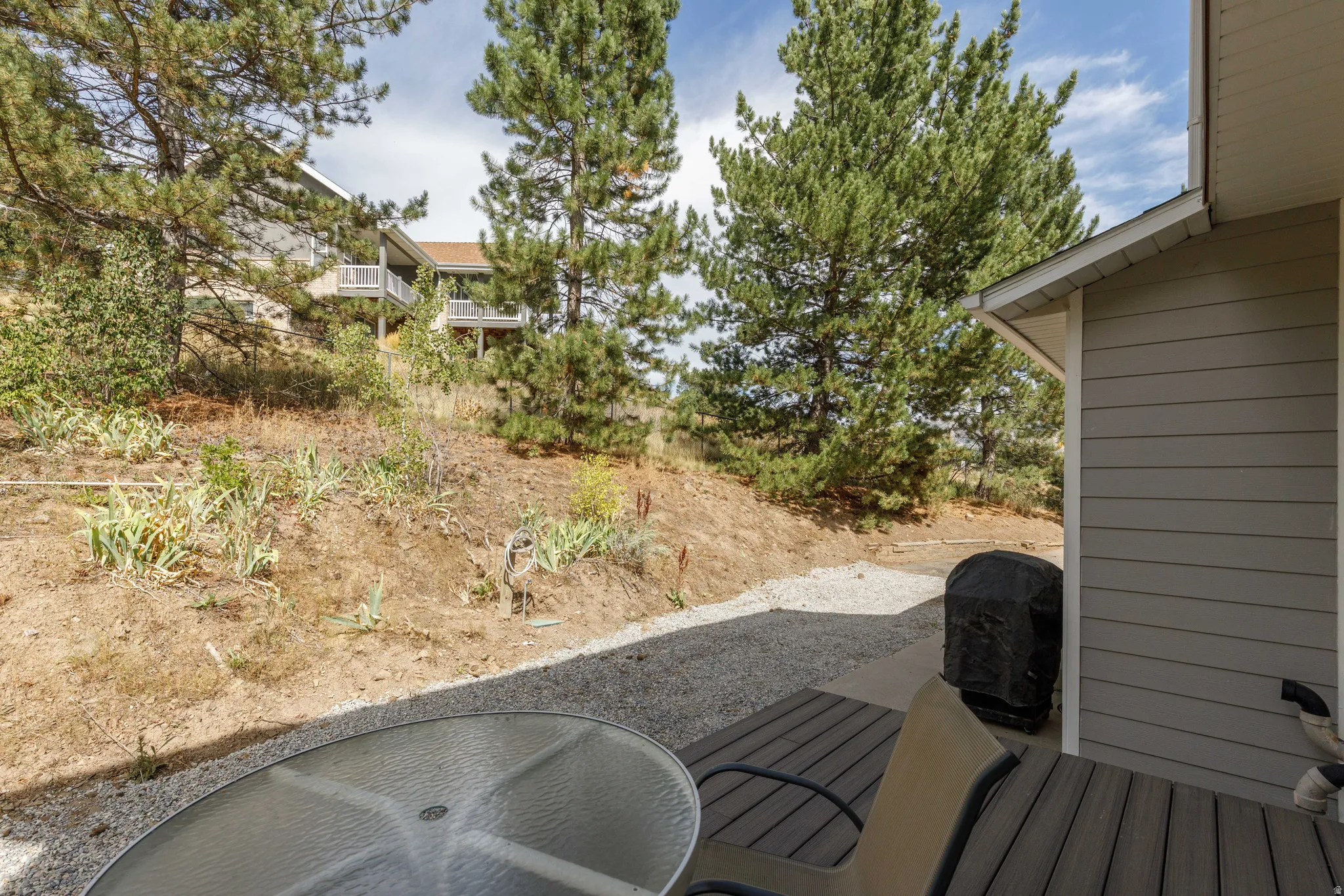 Outdoor deck with wood-finish planks, gravel ground cover, and natural hillside landscaping with mature trees