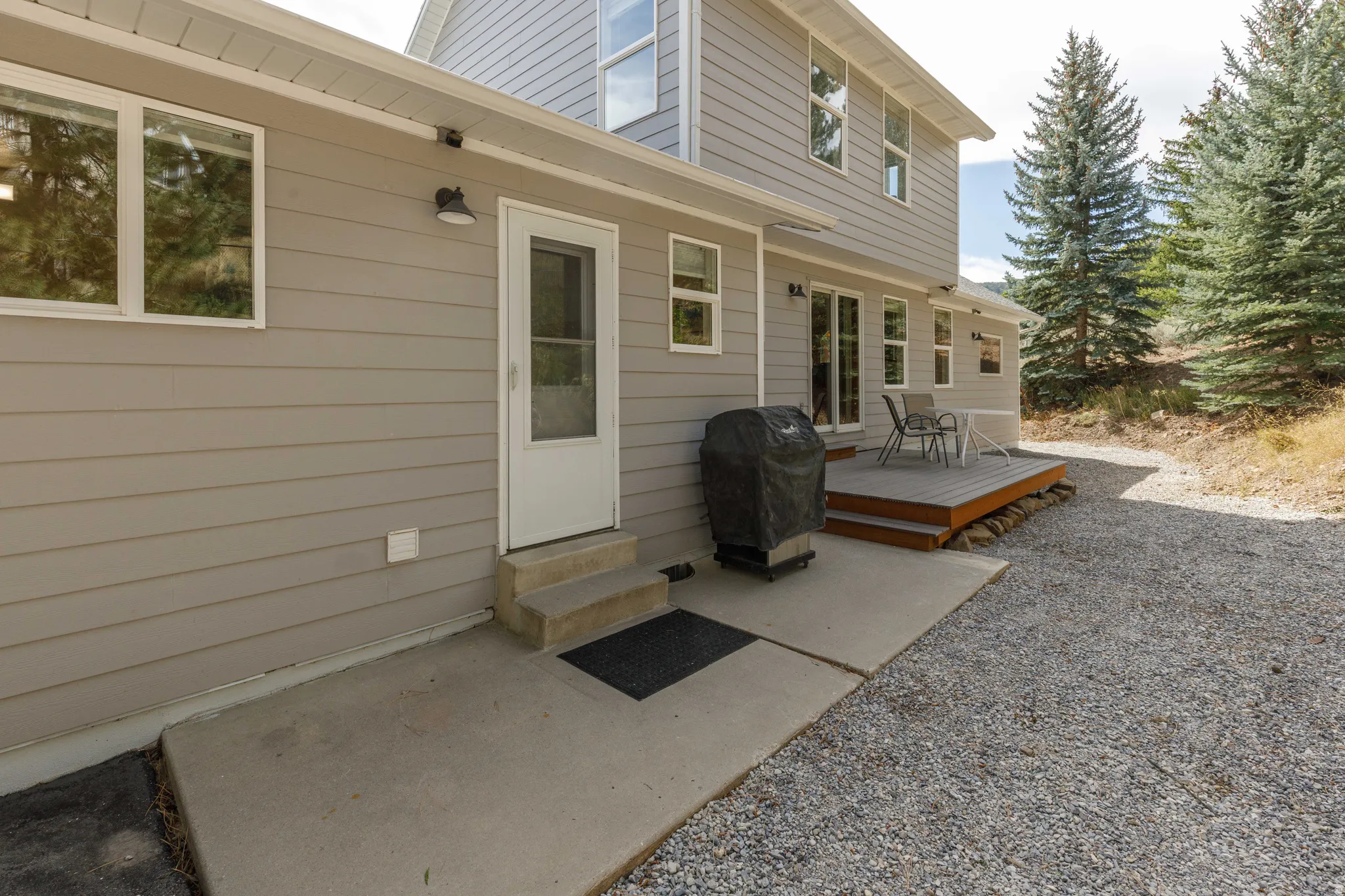 Exterior featuring light gray siding, a raised wood deck, and a concrete patio
