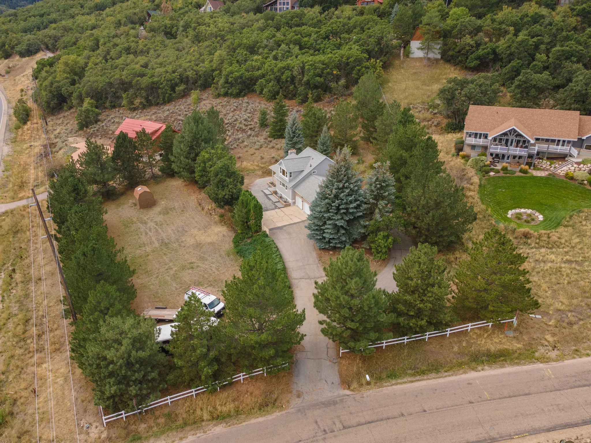 Spacious property featuring a two-car garage, mature trees, a paved driveway, and white perimeter fencing