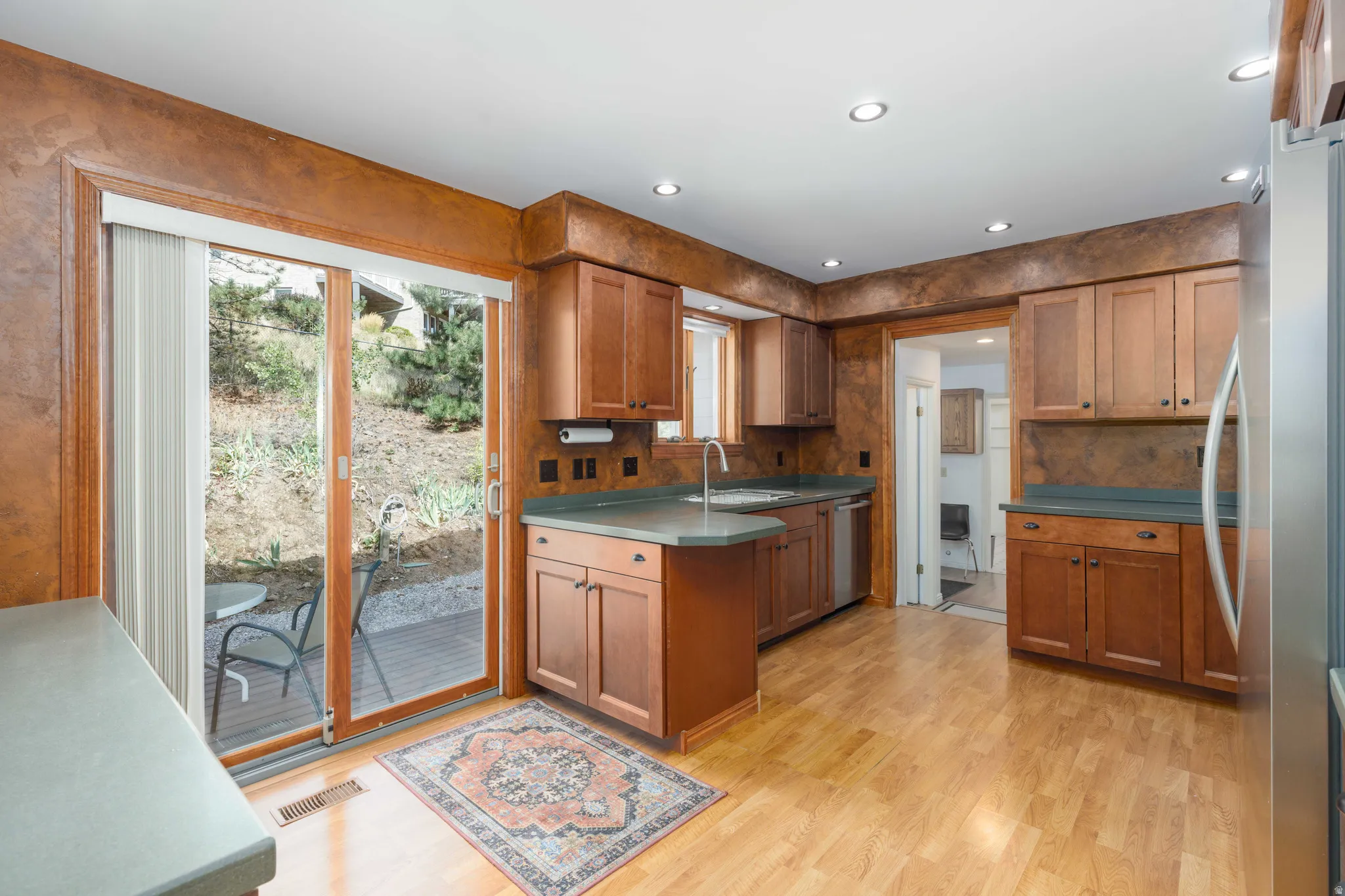 Hardwood-style flooring, recessed lighting, wood cabinetry, stainless steel appliances, and sliding glass doors to outdoor patio
