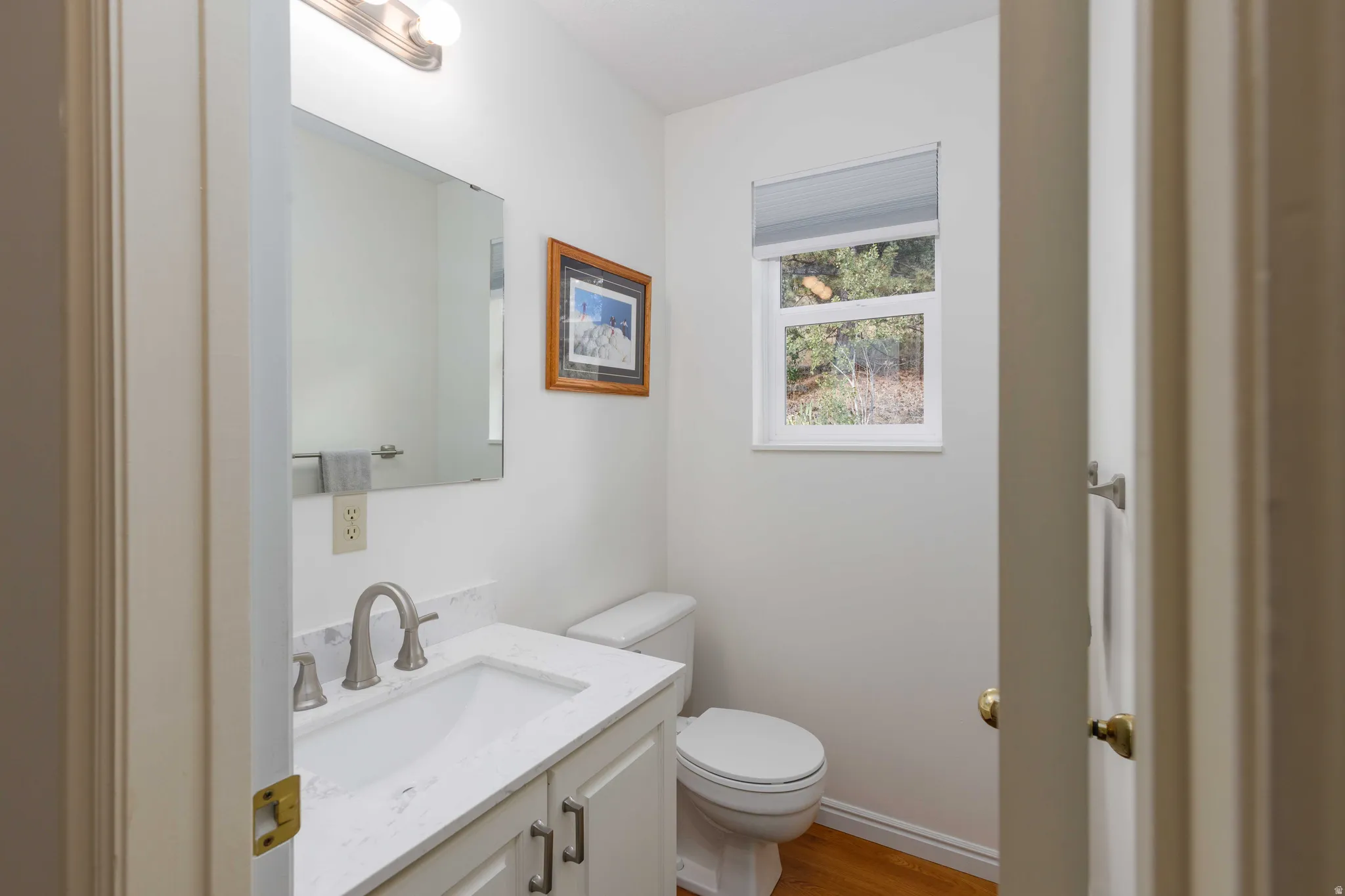 Vanity with a white countertop and undermount sink, brushed nickel faucet, and wood-finish flooring