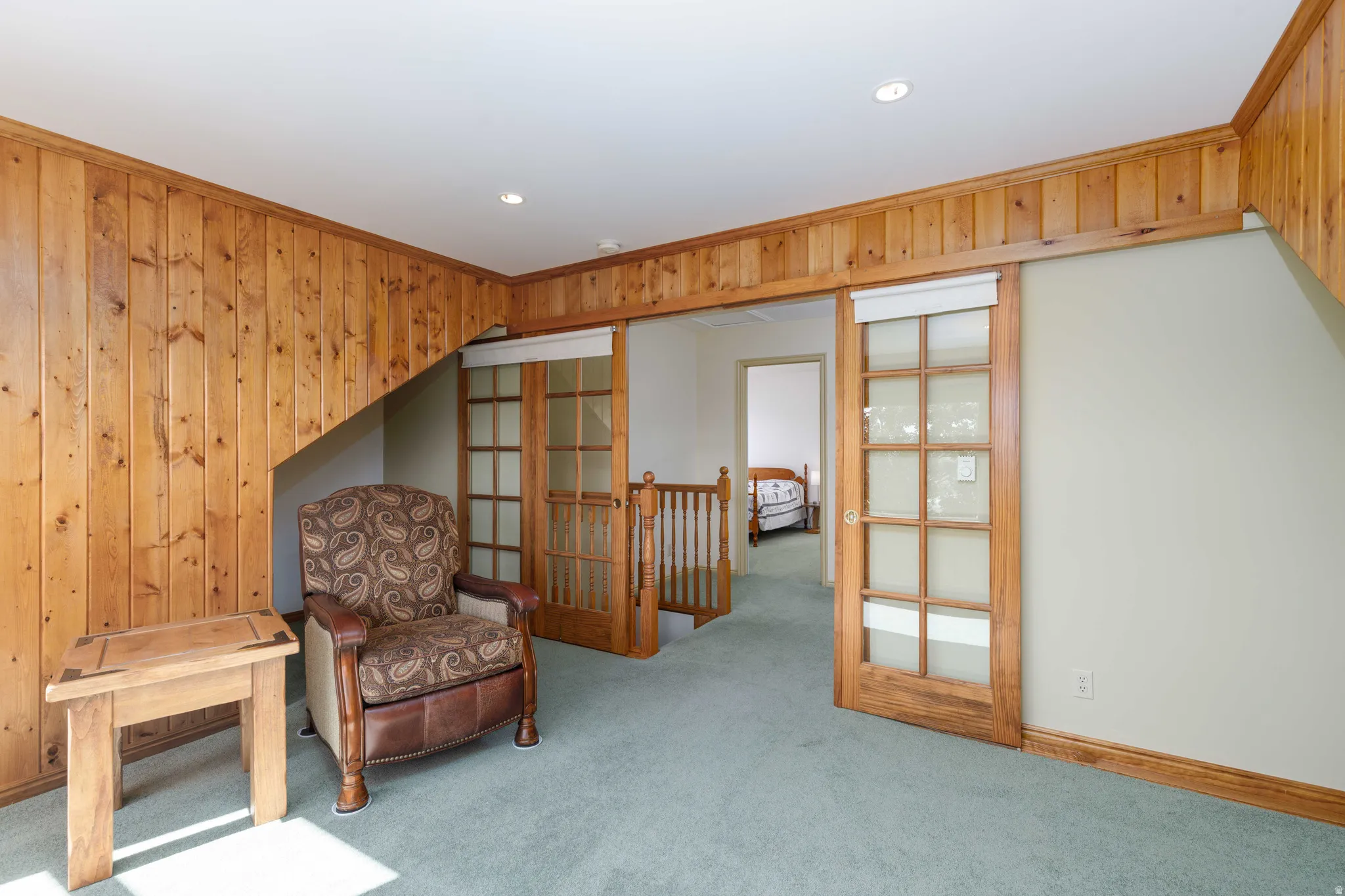 Wood-paneled accent wall, wood-finish sliding doors with glass panels, recessed ceiling lighting, and light-colored wall paint