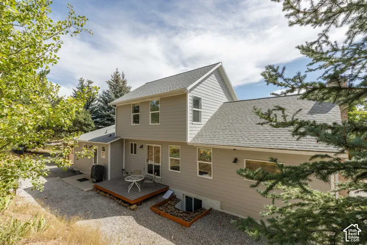 Two-story exterior with light gray siding, a gray shingle roof, and a ground-level wood-deck patio