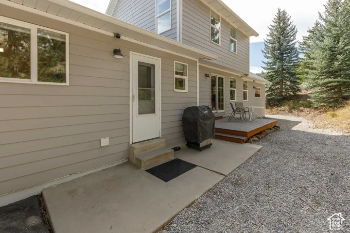 Exterior featuring light gray siding, a raised wood deck, and a concrete patio