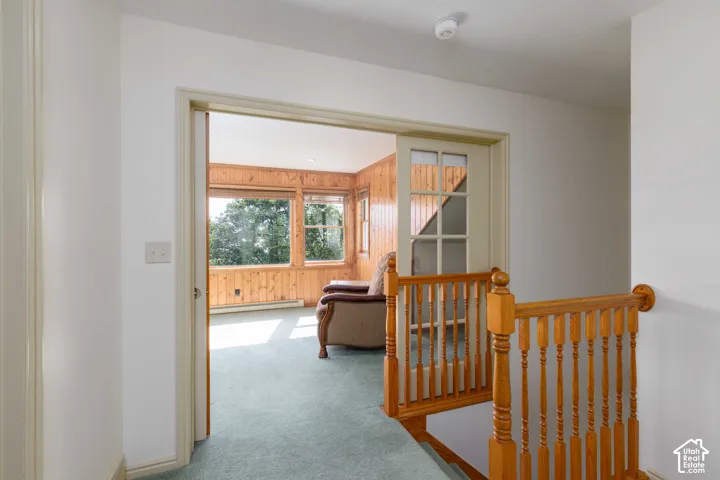 Hardwood stair railing, carpeted flooring, wood paneling, multiple windows, and a panel-glass door