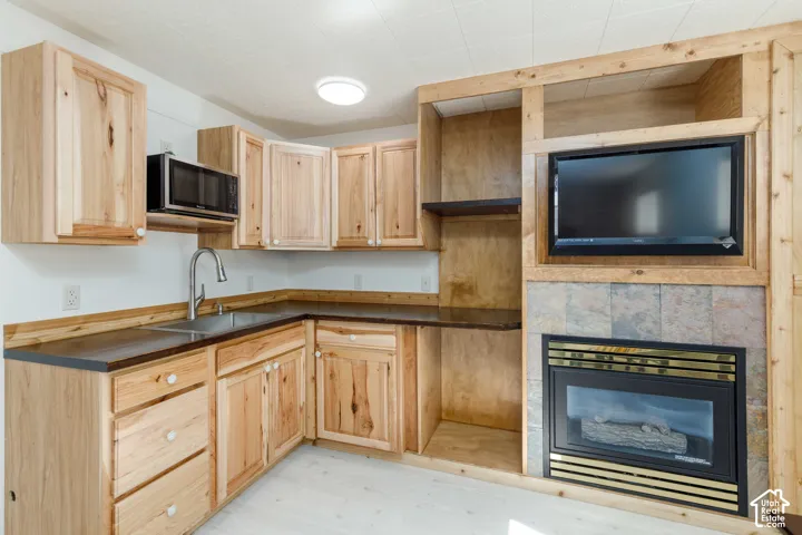 Wood-finish cabinetry, dark countertops, integrated microwave, built-in media center, and a fireplace with tile surround